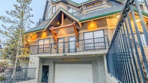 A multi-story building with a garage, balconies, and a metal fence. - "Alpine Hideaway" at Alpine Village (Canmore)