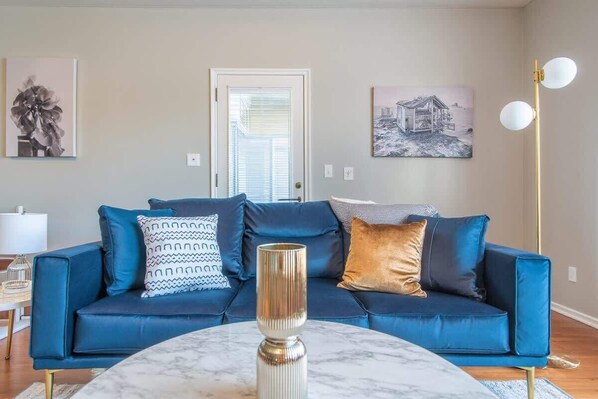 Un salón con un sofá azul, una mesa de centro de mármol y dos lámparas de pared.