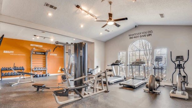 Ein Fitnessstudio mit verschiedenen Trainingsgeräten, motivierenden Texten an der Wand und einem großen Fenster.