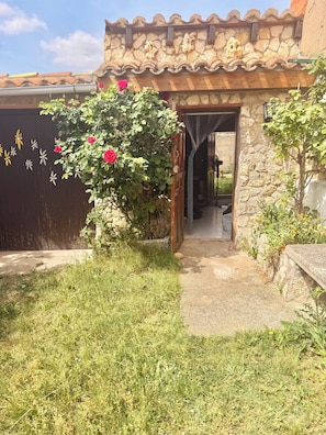 A stone building with a tiled roof, a wooden gate, and a pathway leading to an interior space.