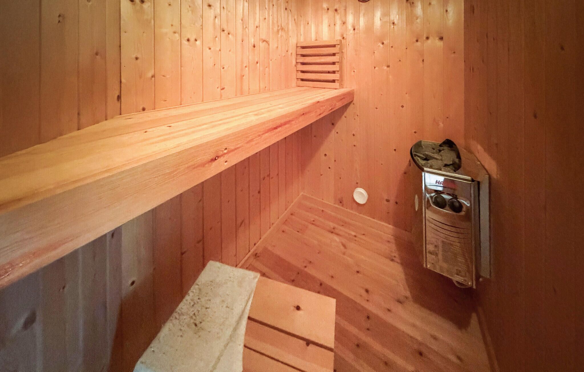 Een houten sauna met een bankje, een klein plankje en een metalen bak.