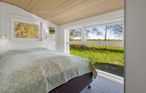 Ein Schlafzimmer mit einem Bett, einem Fenster und Blick auf ein grünes Feld.