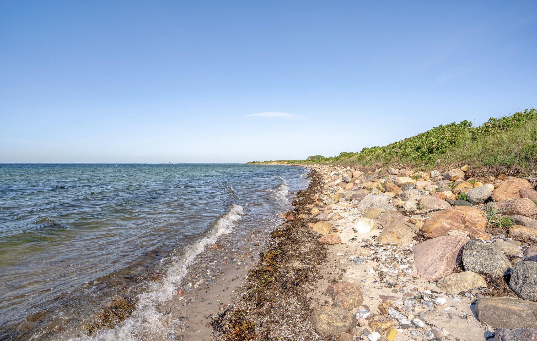 Una costa rocciosa con acque cristalline, un orizzonte lontano e vegetazione sulla destra.