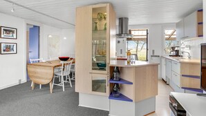 Una cucina moderna con un'isola centrale, un'area pranzo con un tavolo e sedie in legno, e vista all'esterno.