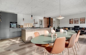 A modern kitchen with a central island, a dining area with a round table and chairs, and a living area with a sofa and artwork on the wall. - Beautiful home in Sydals with WiFi (Sydals)