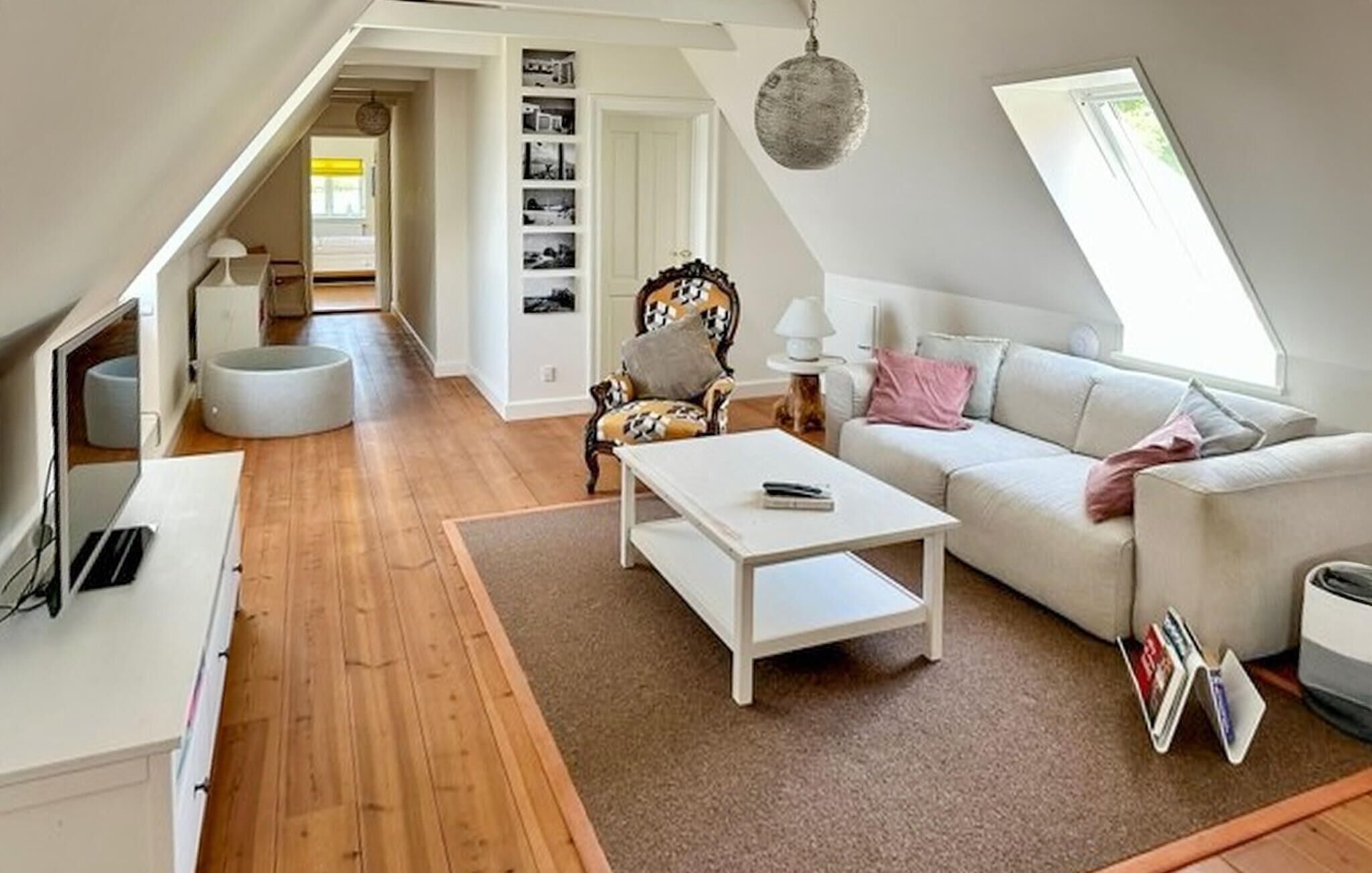 Een modern loft appartement met een hoge plafond, een witte bank, een salontafel, een gestreept fauteuil en een boekenkast.