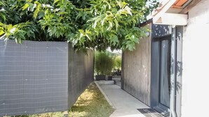 A narrow pathway leading to a building with a dark door and a fenced area with a tree. - Lovely home in Saint-Vincent-de-Paul (Saint-Vincent-de-Paul)