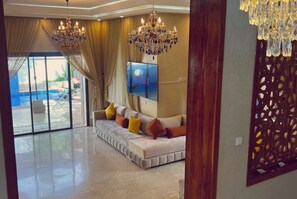 A spacious living room with a large sofa, a TV, and two chandeliers.