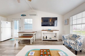 A modern living room with a wooden bench, a white desk, a patterned armchair, and a flat-screen TV mounted on the wall. - TL710 Private Pool, Charcoal Grill, Parking for 2 (Port Aransas)