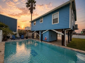 A residential setting with a swimming pool, a blue house, and a palm tree. - TL710 Private Pool, Charcoal Grill, Parking for 2 (Port Aransas)