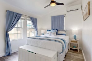 A bedroom with a bed, curtains, a nightstand, a lamp, a ceiling fan, and an air conditioning unit. - TL710 Private Pool, Charcoal Grill, Parking for 2 (Port Aransas)