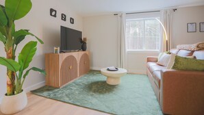 Ein Wohnzimmer mit Fernseher, einer Couch, einem Couchtisch und einer Topfpflanze.