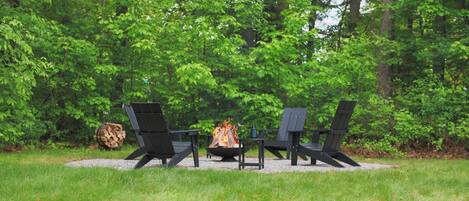 An outdoor seating area with two Adirondack chairs, a fire pit, and a stack of firewood.