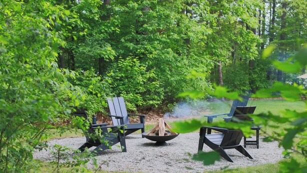 Ein bewaldetes Gebiet mit Feuerstelle und Adirondack-Stühlen.