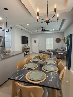A modern dining area with a marble table, beige chairs, and a chandelier.