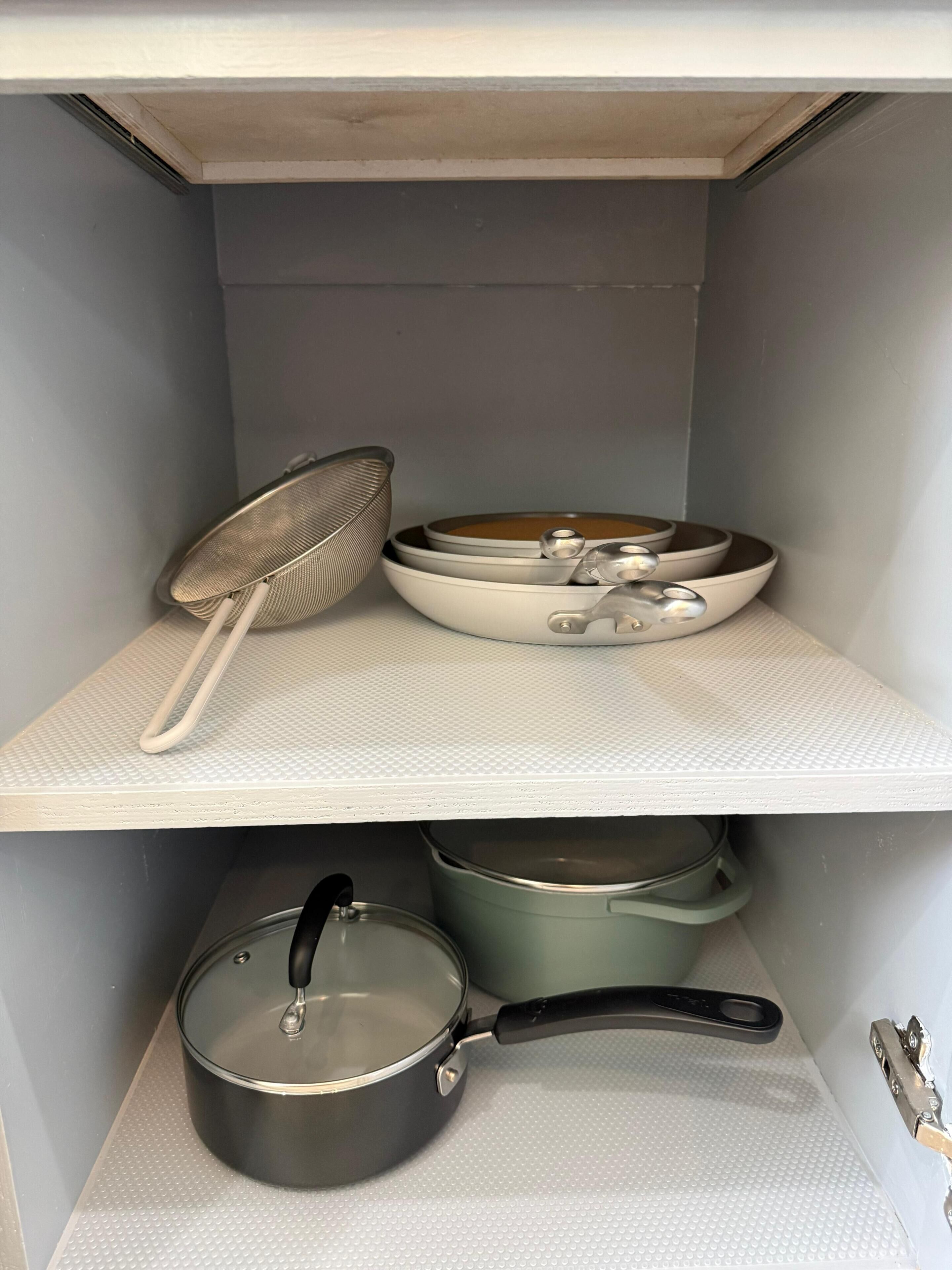 A kitchen pantry with shelves holding cookware, including pots, pans, and a strainer.
