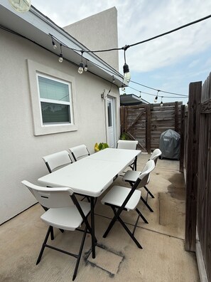 A patio with a white table and chairs, a wooden fence, and string lights.