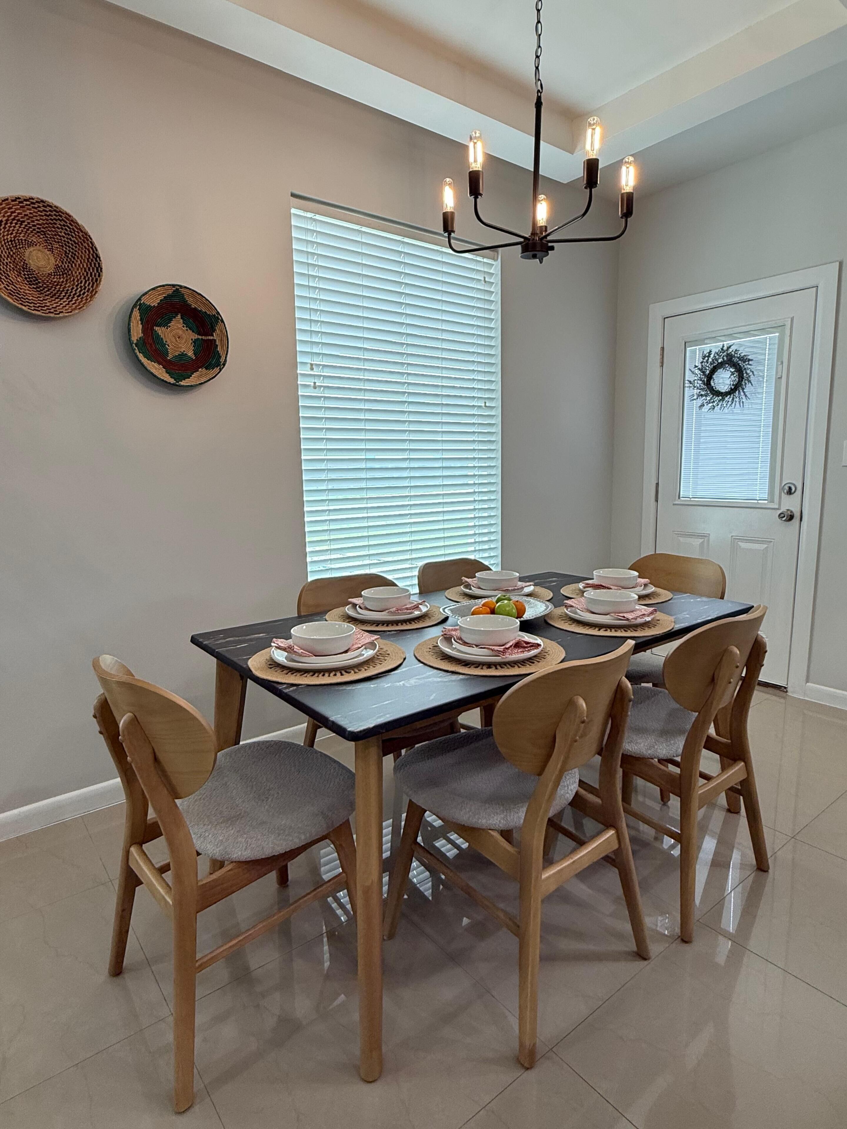 A dining area with a table set for six, surrounded by wooden chairs with grey cushions.