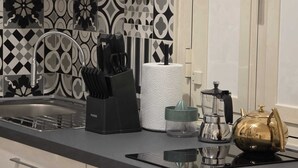 A kitchen with a black and white patterned backsplash, a stainless steel sink, a knife block, a paper towel holder, a green container, a glass carafe, and a gold-colored teapot. - Townhouse 41 - Trieste - by Be Your Home (Civitavecchia)