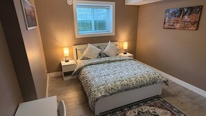 Een slaapkamer met een bed, twee bedlampen, een raam, een schilderij, een bureau en een stoel.