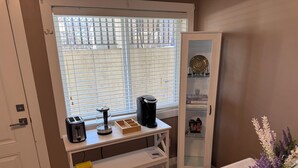 Een kamer met raam, koffiezetapparaat, een kast met glazen deuren en een vaas met bloemen.
