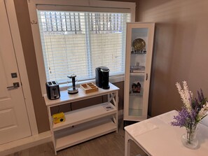 Ein Zimmer mit Fenster, einer Kaffeemaschine, einem Schrank mit Glastüren und einer Vase mit Blumen.