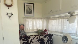 A compact RV interior with a dining table, a small fan, a trash can, and a cow-print cushion. - Dale-Vintage Glamping at Winery Near Sequoia (Dunlap)