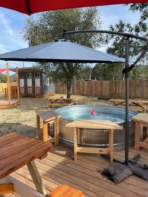 Un patio trasero con jacuzzi, terraza de madera, mesas de picnic y un cobertizo pequeño.