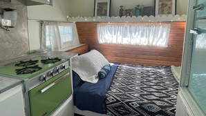 A compact RV interior with a kitchenette, a bed with patterned bedding, and a window with curtains. - Dale-Vintage Glamping at Winery Near Sequoia (Dunlap)