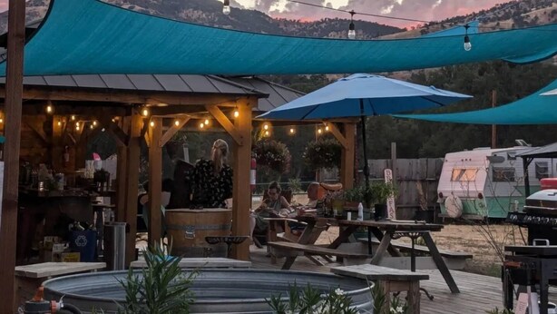 An outdoor patio area with tables, umbrellas, and string lights against a backdrop of mountains and a sunset sky. - Dale-Vintage Glamping at Winery Near Sequoia (Dunlap)