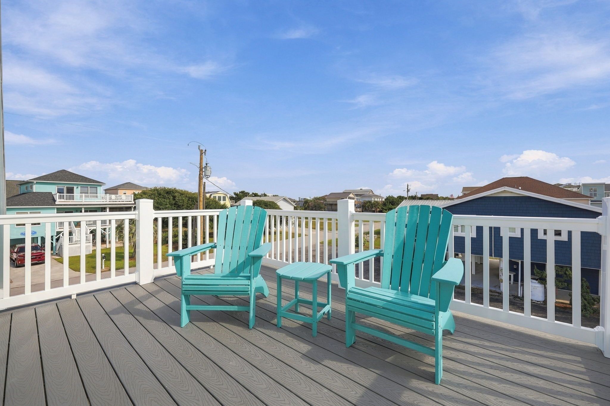 A wooden deck with two chairs and a table, surrounded by a white fence, overlooking a residential area.