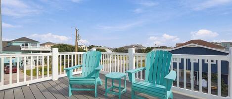 A wooden deck with two chairs and a table, surrounded by a white fence, overlooking a residential area.