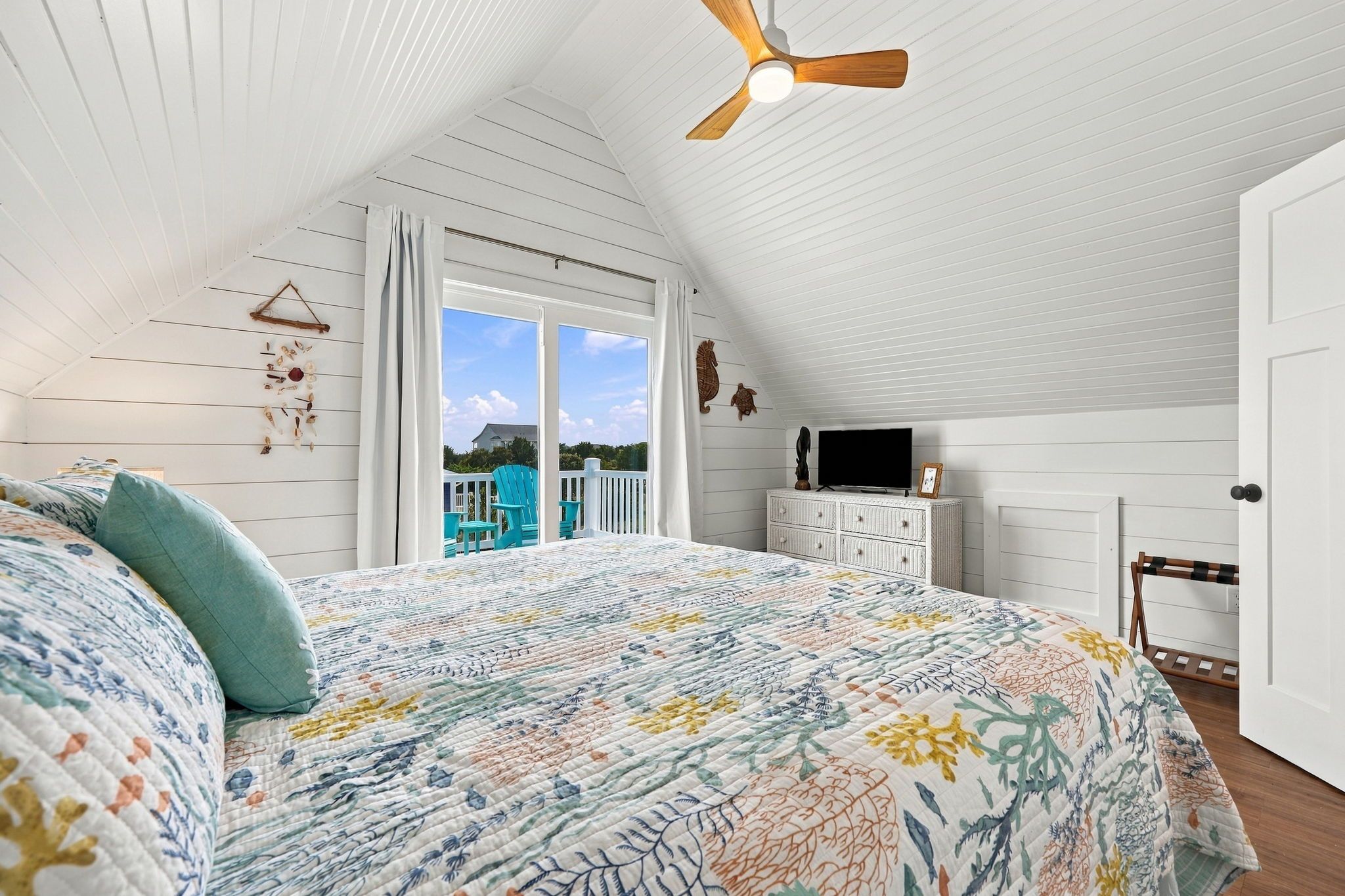A bedroom with a large bed, a ceiling fan, a TV, and a view of the outdoors.