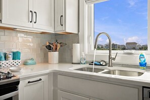 Cozinha com armários brancos, pia de aço inoxidável e janela com vista para casas.