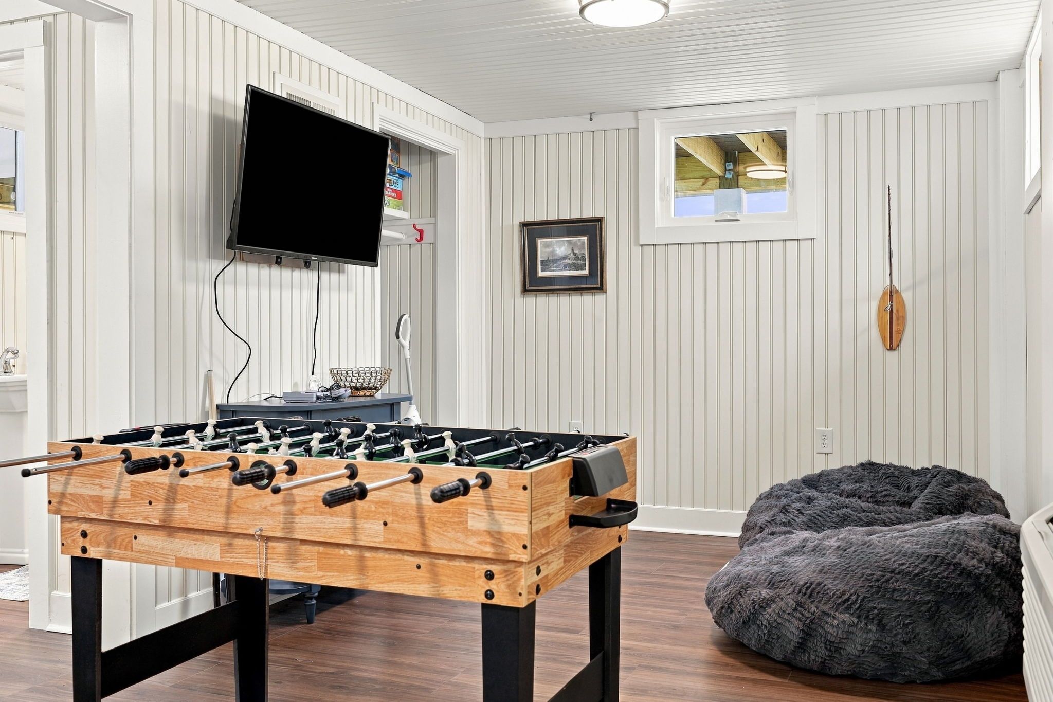 A room with a foosball table, a television mounted on the wall, a framed picture, and a bean bag chair.