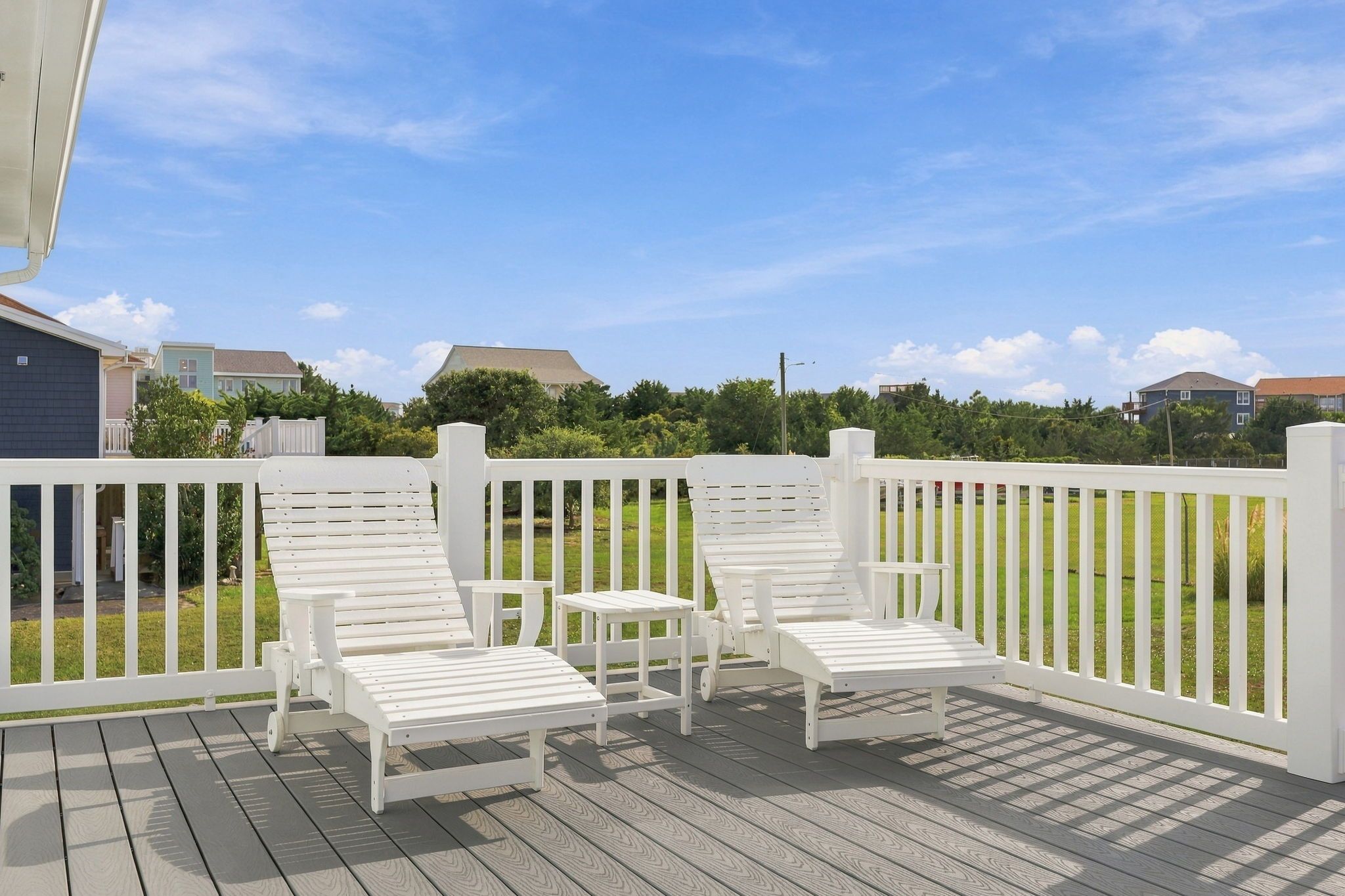 A deck with white railings and two lounge chairs.