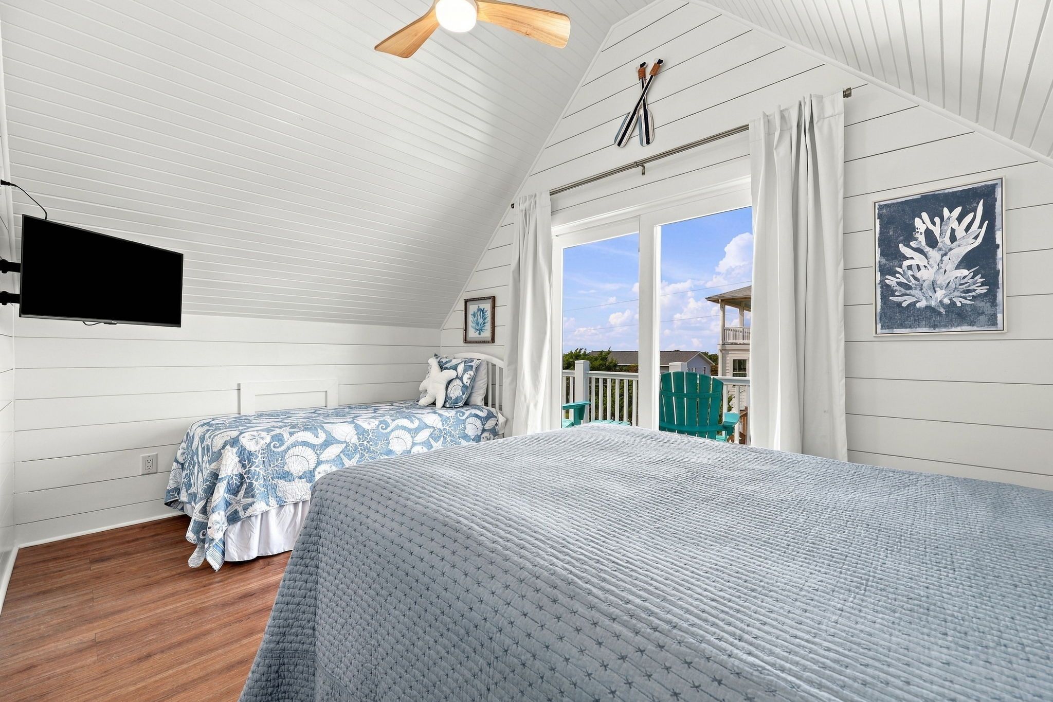 A bedroom with two beds, a ceiling fan, a TV, and a view of the outside.