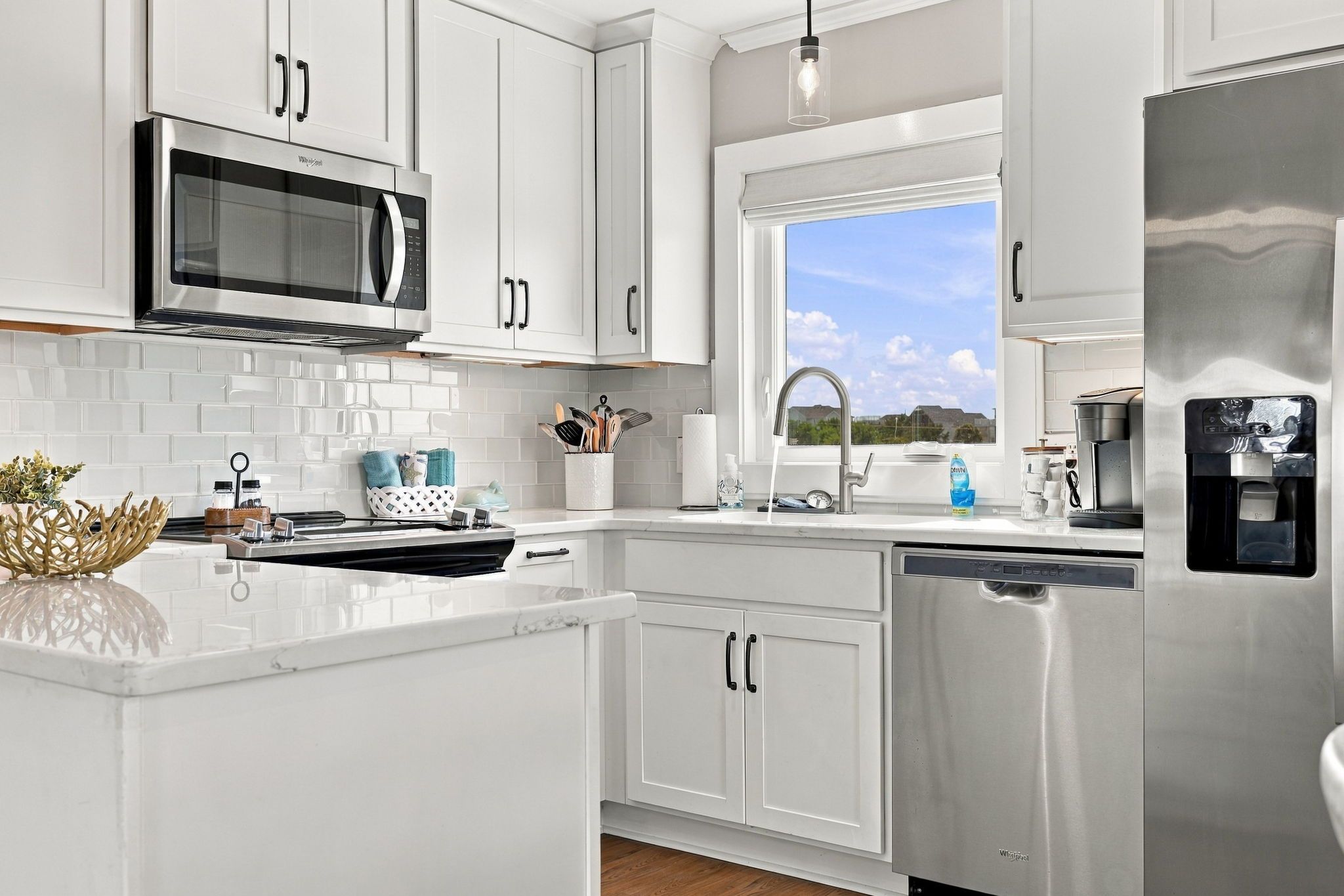 A modern kitchen with white cabinetry, a stainless steel microwave, a dishwasher, and a water dispenser.