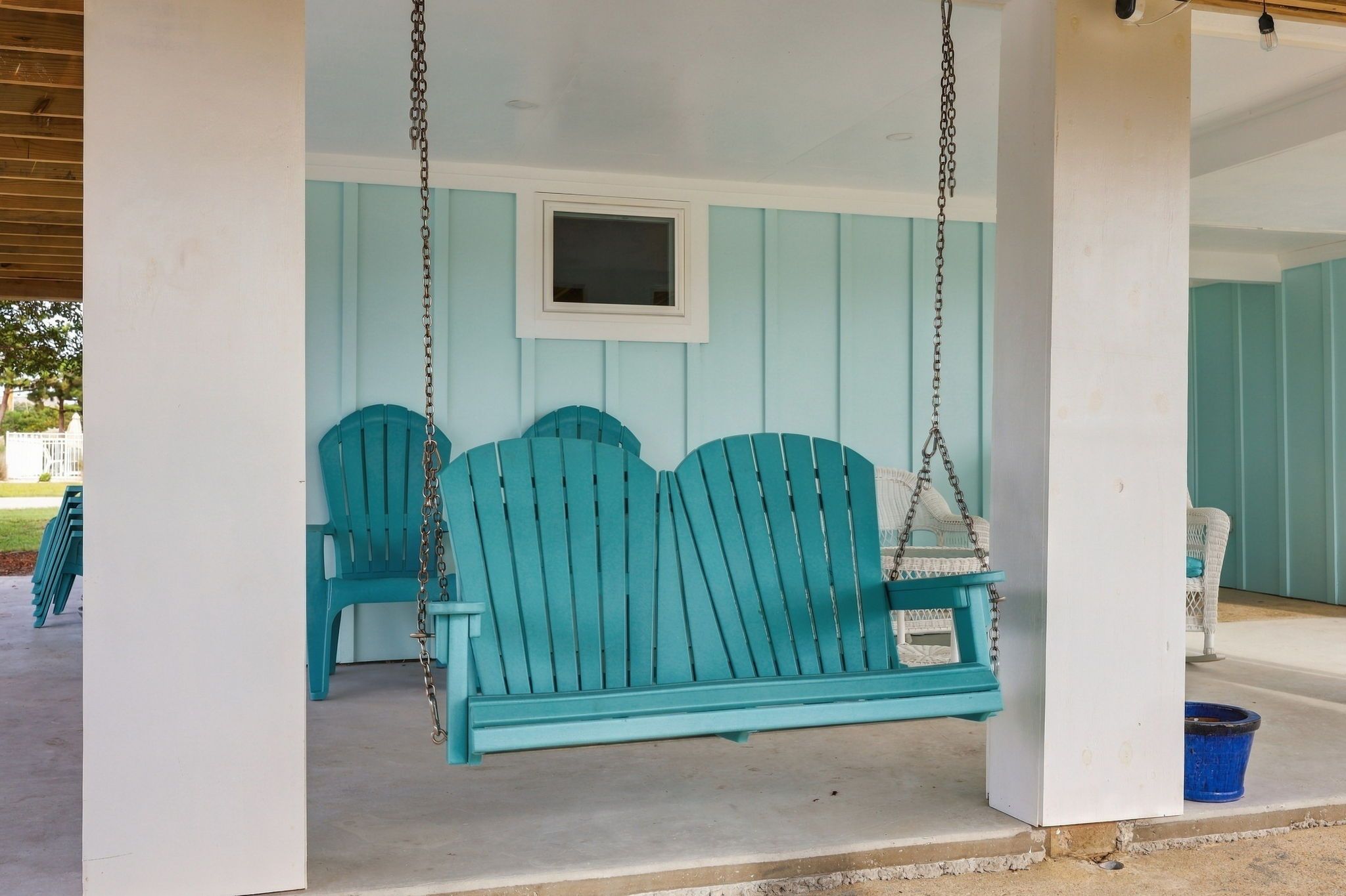 A porch with two turquoise Adirondack chairs and a hanging swing.