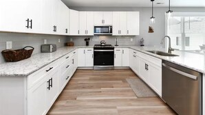 Une cuisine moderne avec des meubles blancs, un lave-vaisselle en acier inoxydable, un four à micro-ondes et un four encastré.