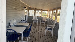 En overdækket veranda med et bord, stole, en lygte og lyskæder.