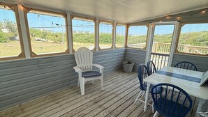 En overdækket træterrasse med et bord, stole og udsigt over landskabet.