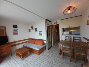 Ein gemütlicher, kleiner Wohnbereich mit einer Couch, einem Holztisch, Stühlen, einem Fernseher und einer Küchenzeile.