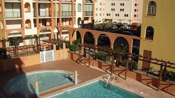 Area piscina con una vasca circolare, pergole in legno e un edificio con balconi sullo sfondo.