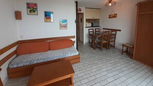 Un ambiente compatto con divano, tavolo da pranzo con sedie, angolo cottura e un piccolo armadio.