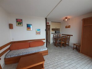 Ein gemütlicher, kompakter Wohnbereich mit einer Couch, einem Esstisch mit Stühlen, einer Küchenzeile und einem kleinen Schrank.