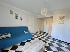 A room with a blue sofa, a checkered floor, a white pendant light, and a door leading to another room. - CAP D'AGDE - Plage du Môle / Réf 319 (CAP D'AGDE)