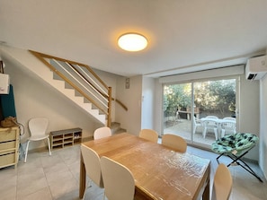 A dining area with a wooden table and chairs, a staircase, and a sliding glass door leading to an outdoor patio with chairs. - CAP D'AGDE - Plage du Môle / Réf 319 (CAP D'AGDE)