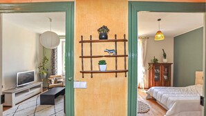A room with a bed, a TV, a shelf with plants, and a door leading to another room. - 1 bedroom beautiful home in Verzeille (Verzeille)