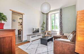 Ein Wohnzimmer mit Fernseher, Sofa, Couchtisch und einer Topfpflanze.